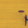 donna con ombrello su muro giallo creativo